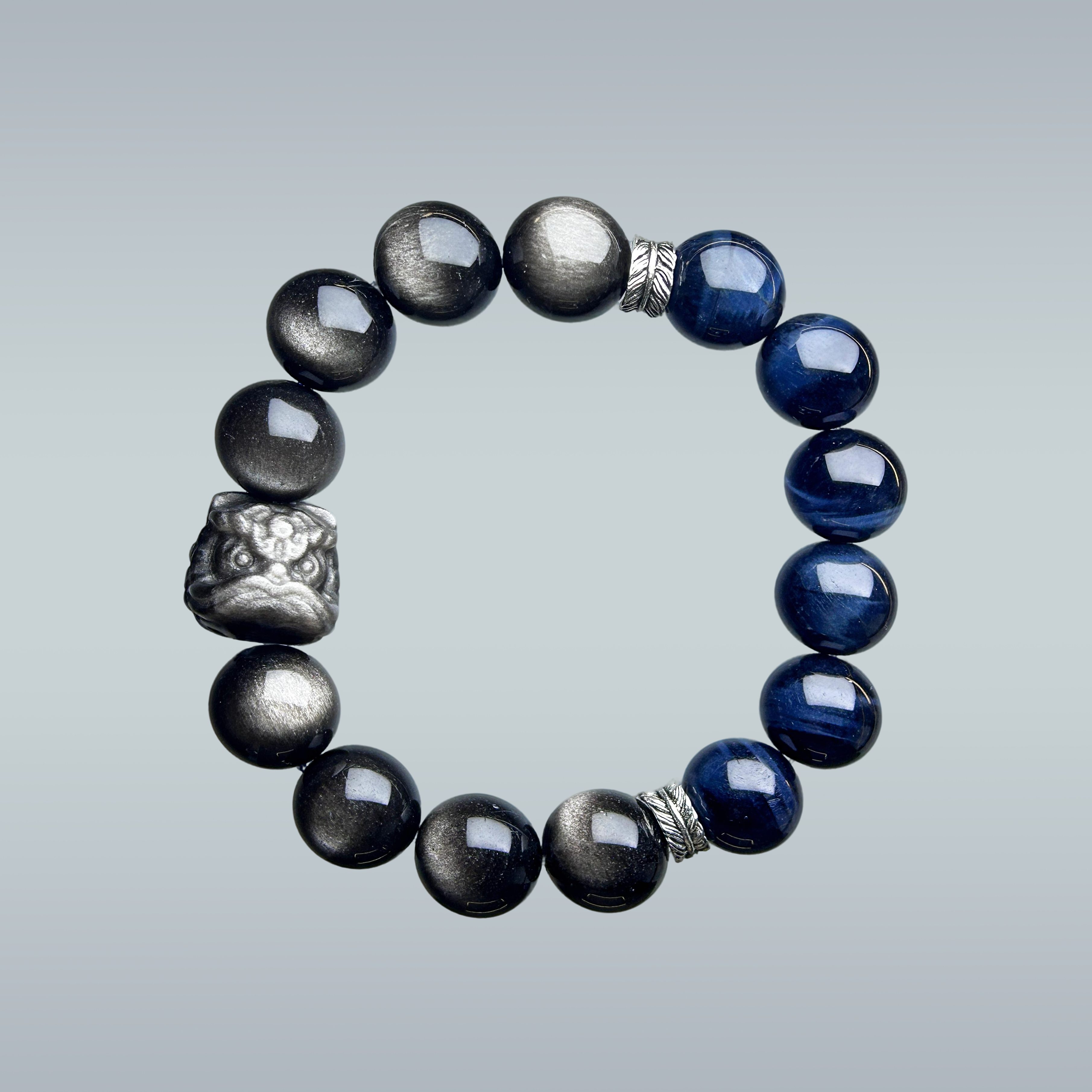 hang lay out of a men bracelet handmade with blue tiger's eye and black obsidian, featuring a pi xiu centerpiece and silver feather spacers.