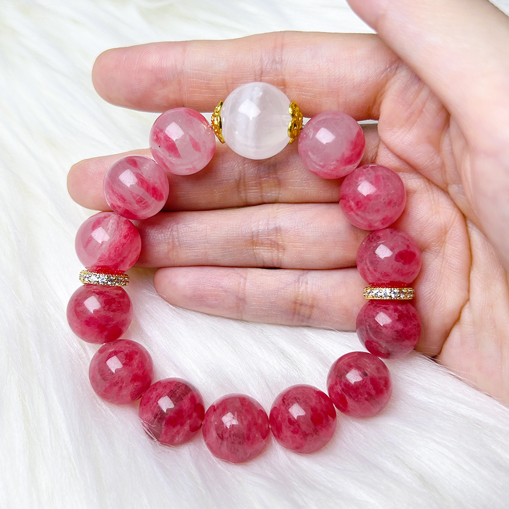 Hand holding pink Rhodonite and Phantom Quartz bracelet with gold and rhinestone accents