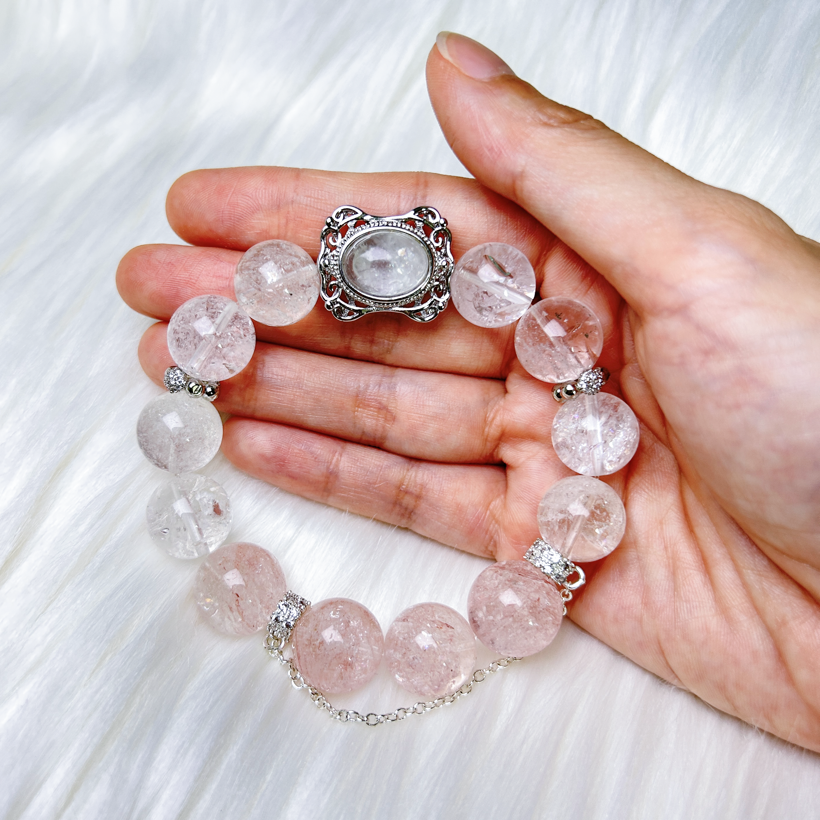 Blossom Valley bracelet featuring rutilated quartz centerpiece with clear and pink azeztulite beads hold on hand.