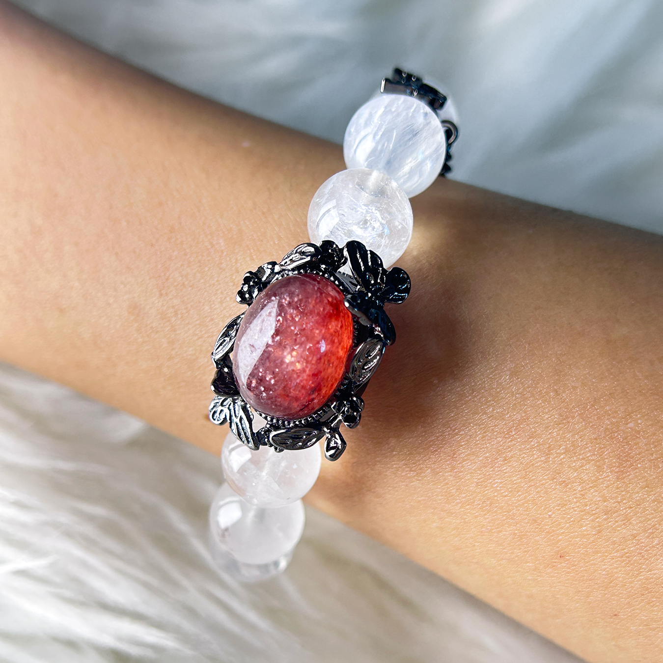 Wrist shot of the sunstone centerpiece on white phantom quartz beads, featuring antique floral detailing and warm gemstone shimmer.