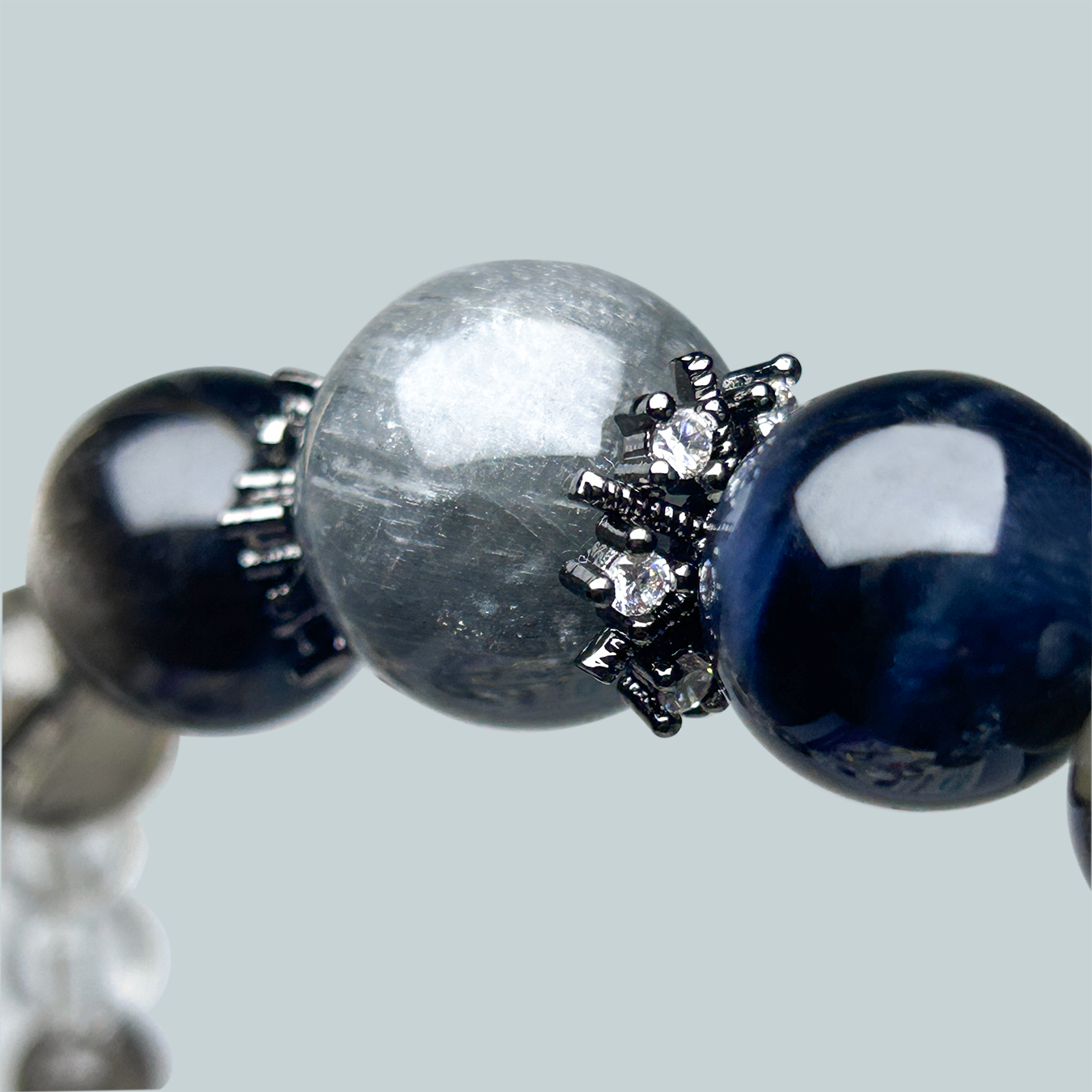 Detail shot of a gray Rabbit Hair Rutilated Quartz bead surrounded by claw-set rhinestone spacers in a crystal bracelet.