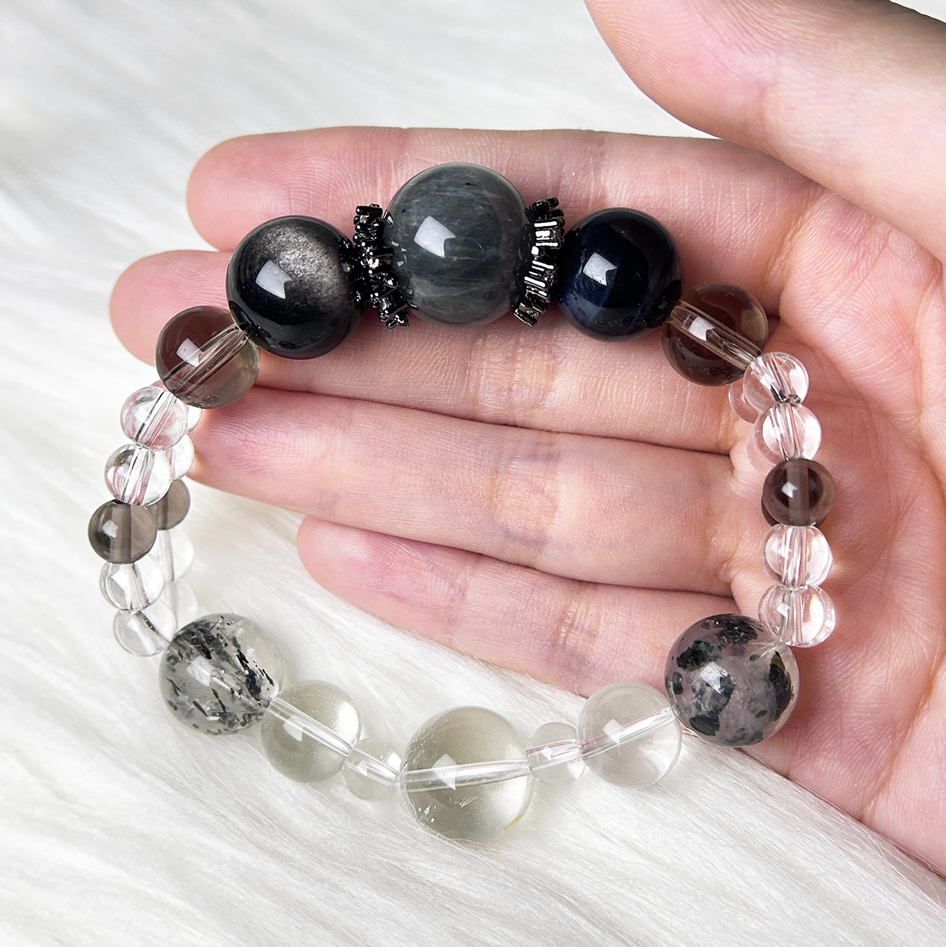 A rabbit hair rutilated quartz centered bracelet with mixed Smoky and clear Quartz beads is displayed in an open hand on soft white fabric.