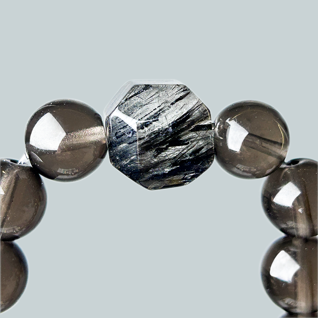 Macro shot of faceted black rutilated quartz gemstone centerpiece in smoky quartz bracelet, showcasing unique needle-like inclusions.