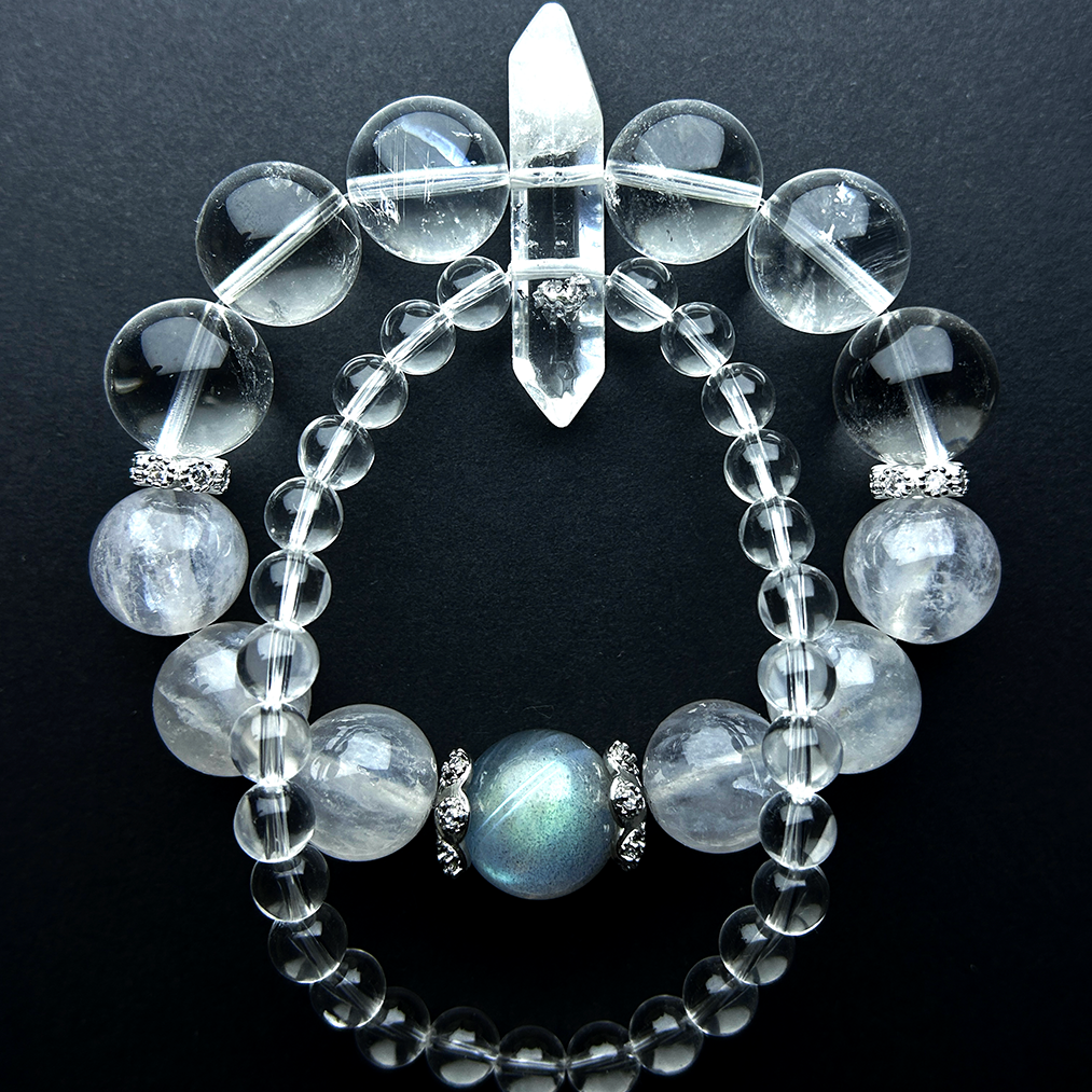 A double layered clear quartz bracelet lay on a black background