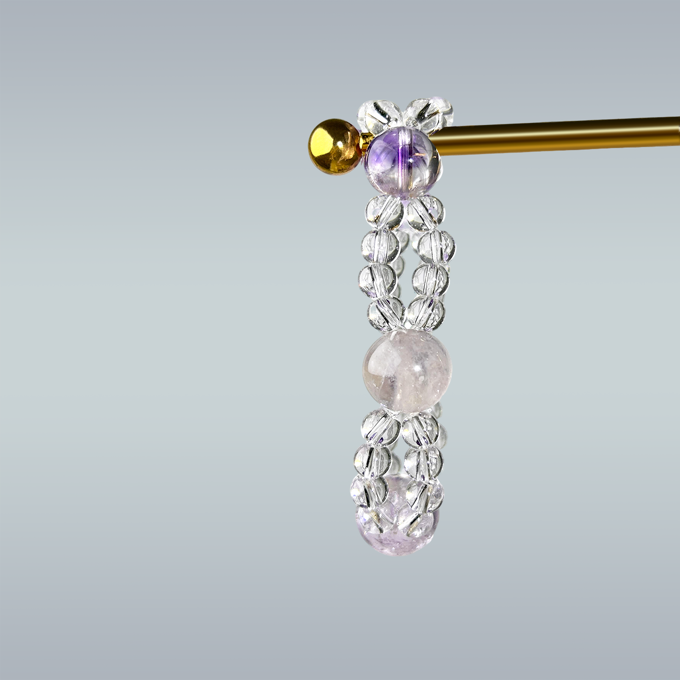 side view of flourite and purple rutilated and clear quartz bracelet on gold stand 