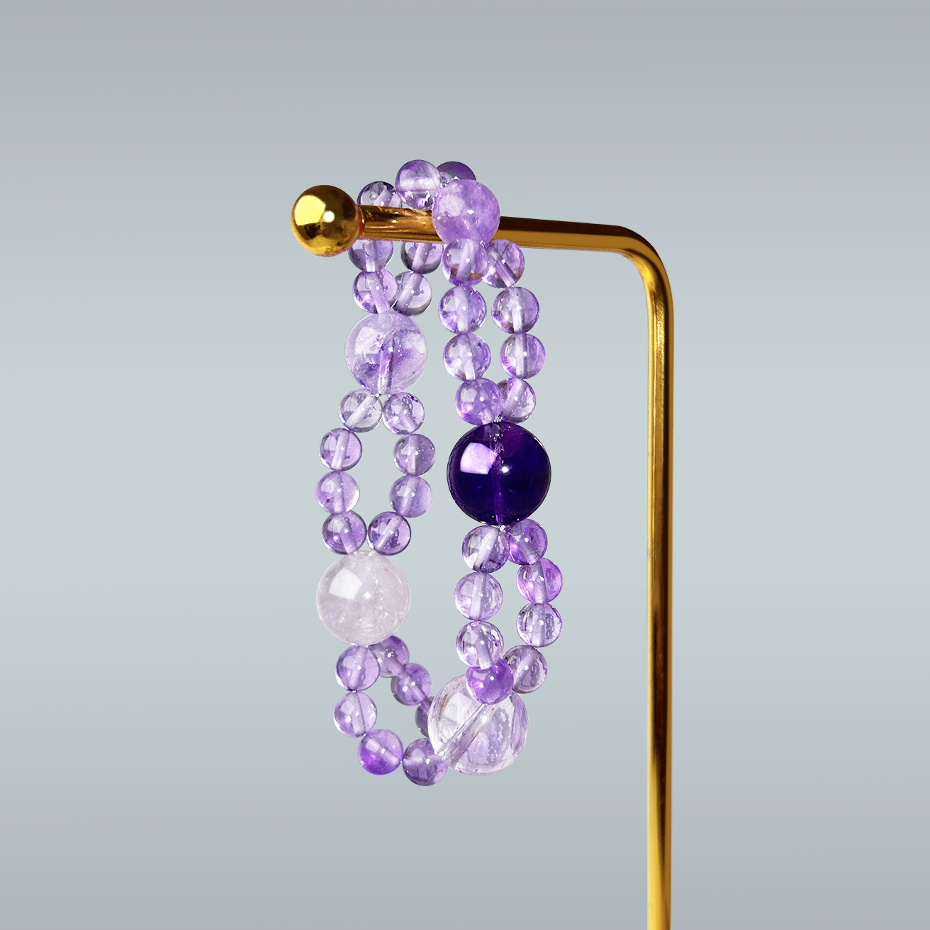 Purple amethyst double layered bracelet hanging on gold metal stand against gray backdrop