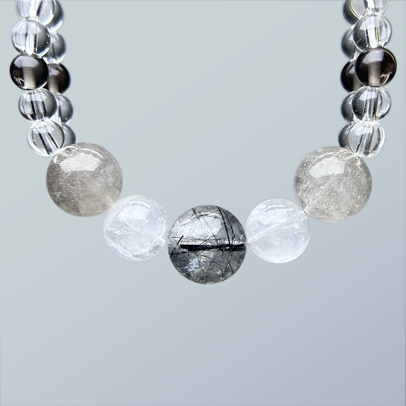 Close-up of crystal bracelet showcasing a center black rutilated quartz bead, flanked by two white phamton quartz and rabbit hair rutilated quartz on a double-row clear quartz strand.