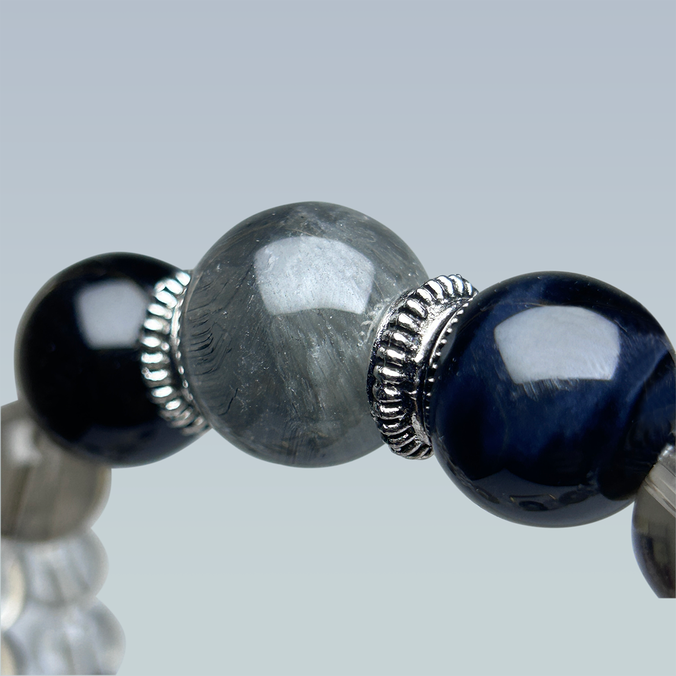 Close-up of a crystal bracelet with Black Obsidian, Blue Tiger’s Eye, and Gray Rabbit Hair Rutilated Quartz centerpiece with silver ring charm.