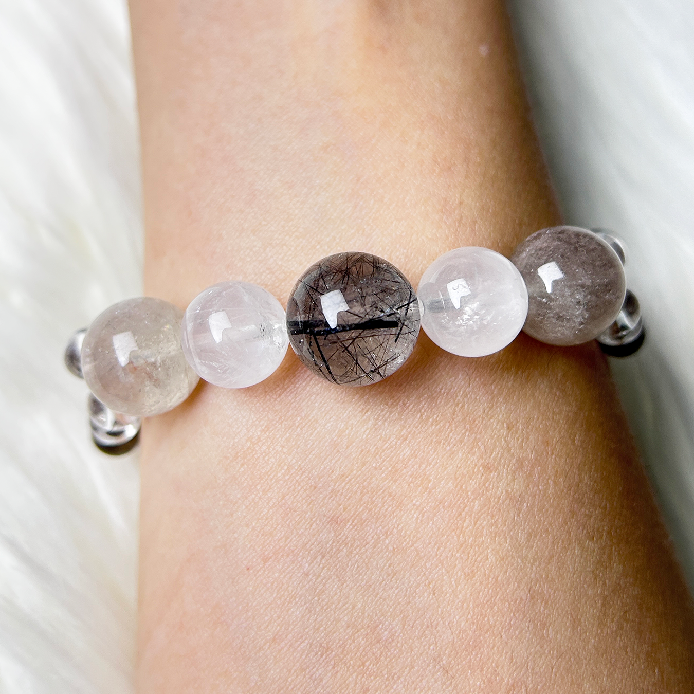 Healing crystal bracelet with black rutilated quartz and white rabbit hair rutilated quartz beads worn on wrist.