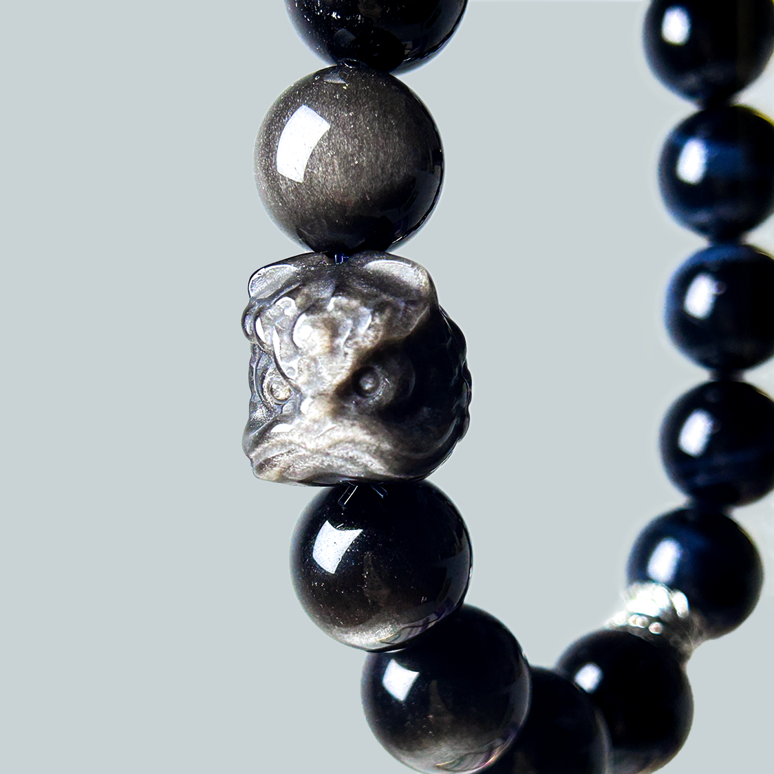 close up shot of the pi xiu centerpiece of a men bracelet made with blue tiger's eye and black obsidian