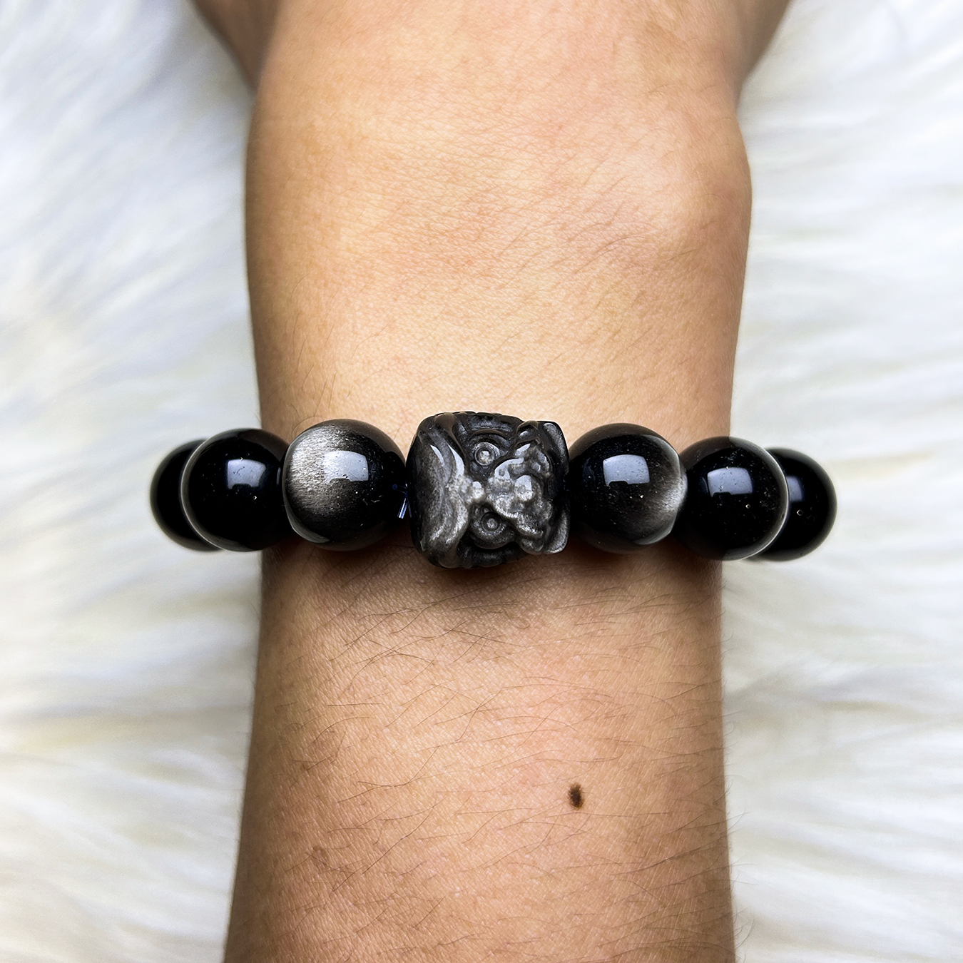 Black obsidian bracelet with a pi xiu centerpiece on a wrist against a white background