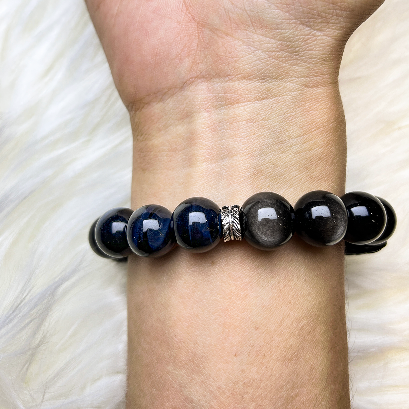 Bracelet with blue tiger's eye and black obsidian beads on a men wrist against a white fabric background