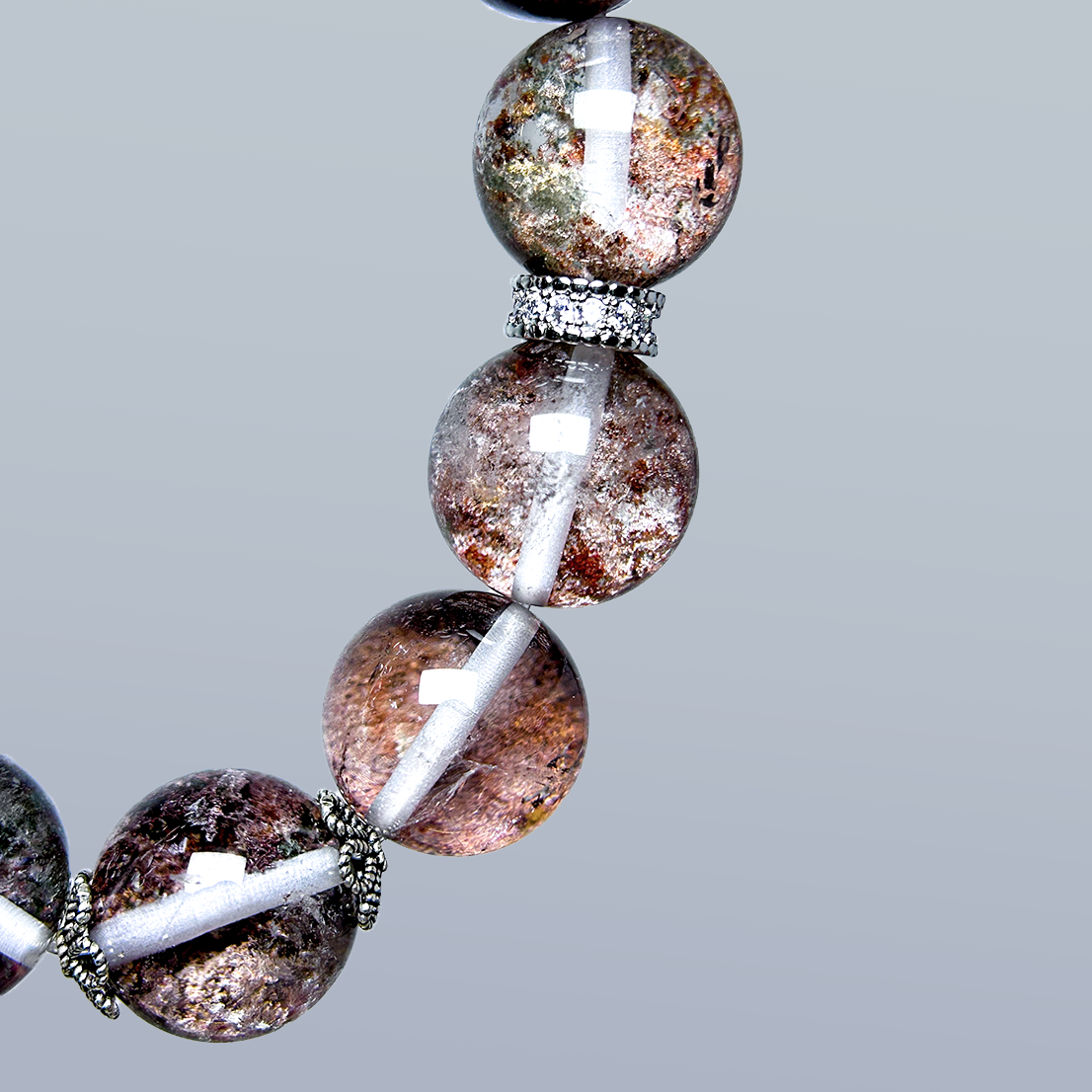 Macro close-up of Phantom Quartz bracelet section, highlighting intricate red, green, and smoky inclusions inside crystal beads.