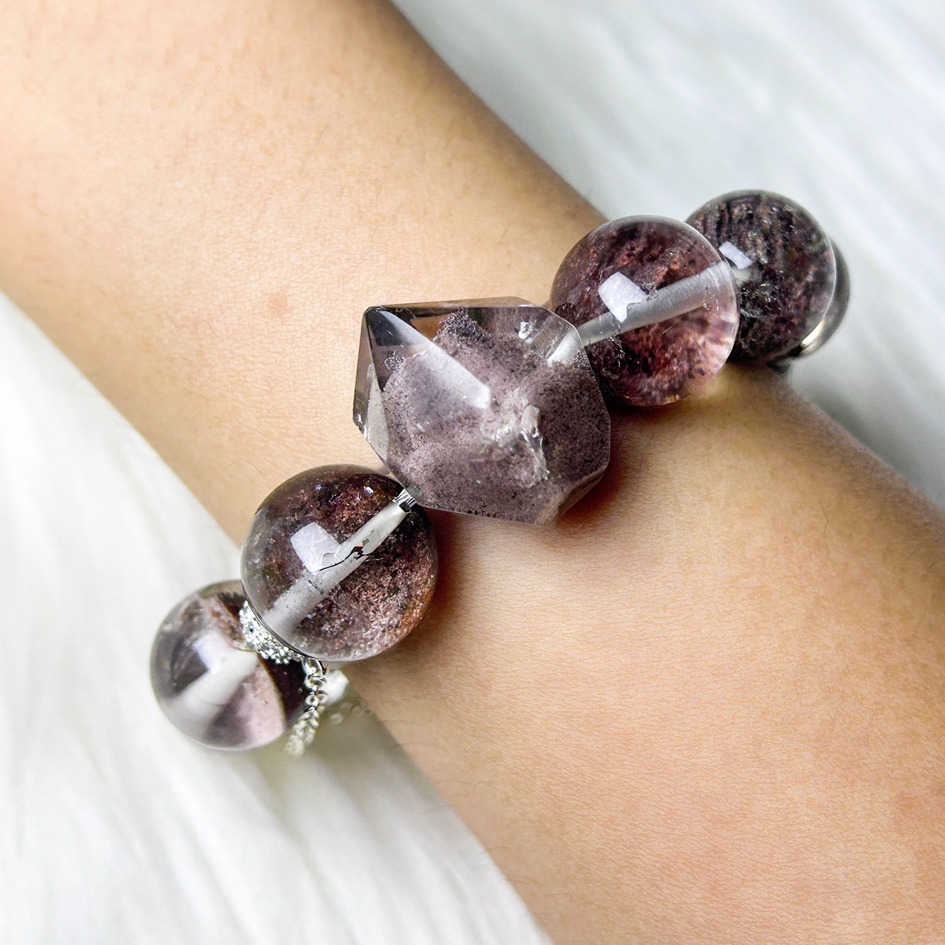 Side view wrist shot of Phantom Quartz bracelet with visible layered inclusions and faceted crystal centerpiece.