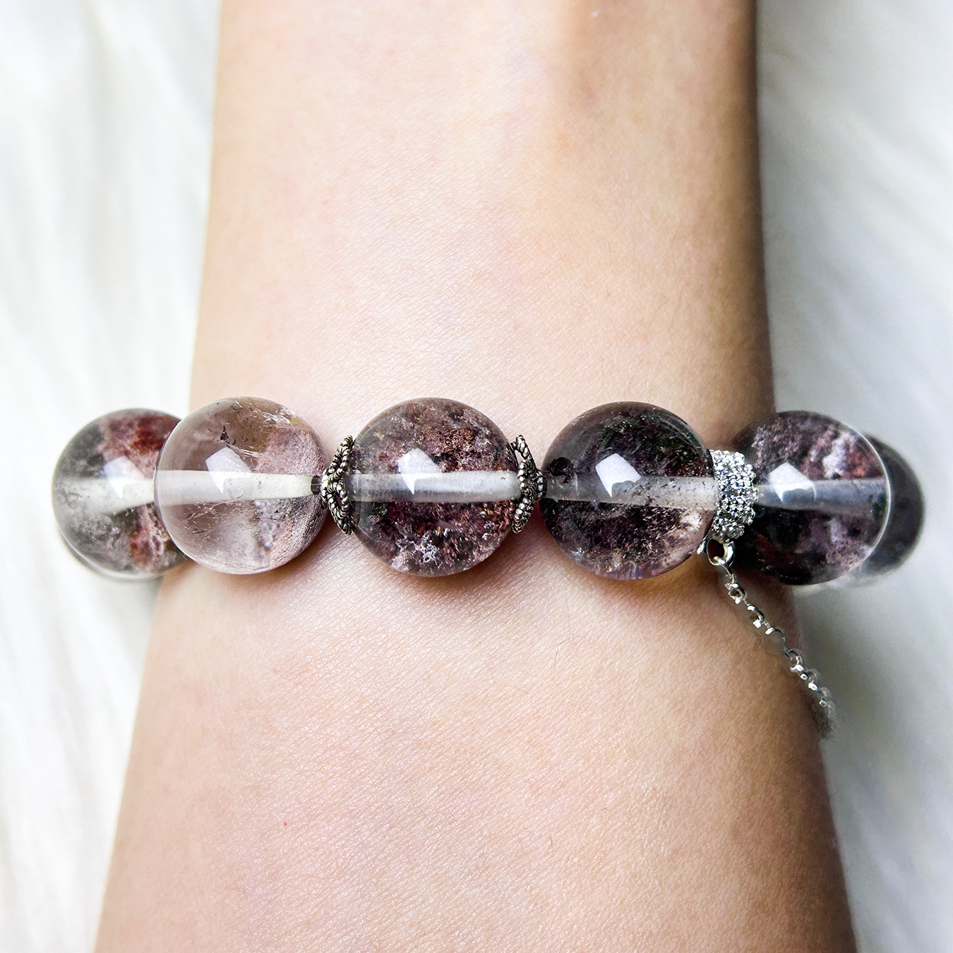Centered view of Phantom Quartz bracelet on wrist, emphasizing bead clarity, earthy hues, and silver floral spacers.