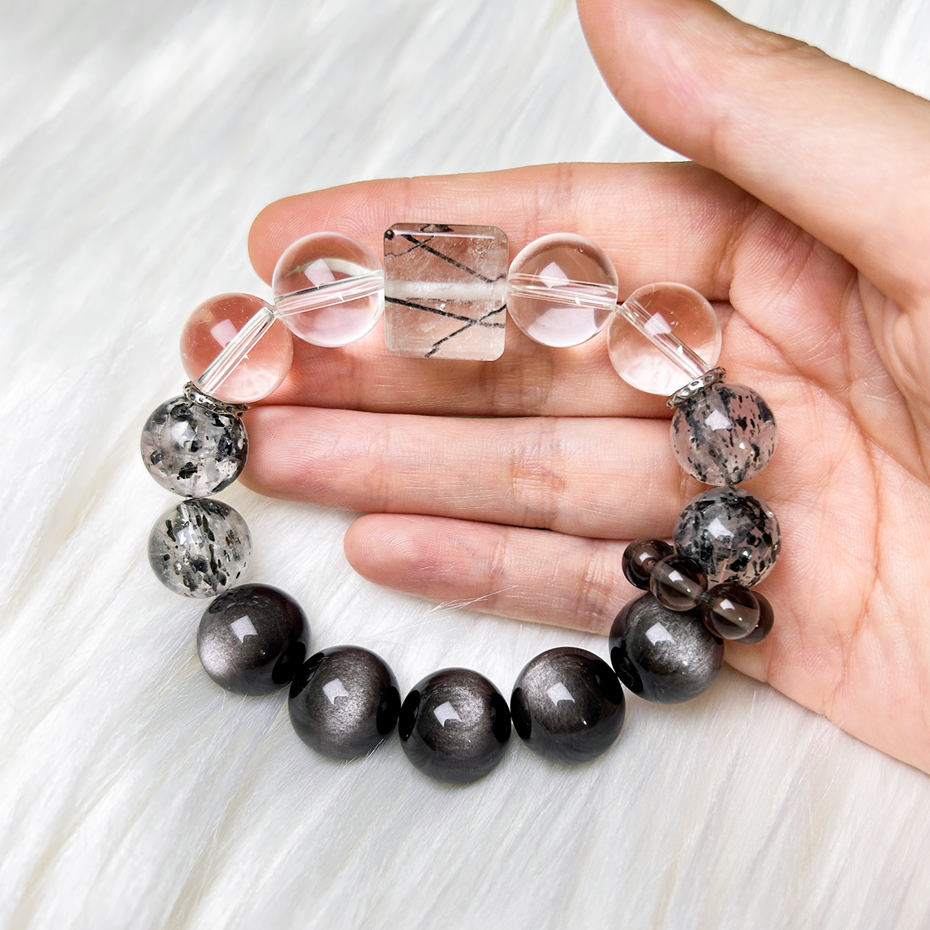 Close-up of Monochrome Vein crystal bracelet with gradient from clear quartz to black obsidian hold on hand in white background