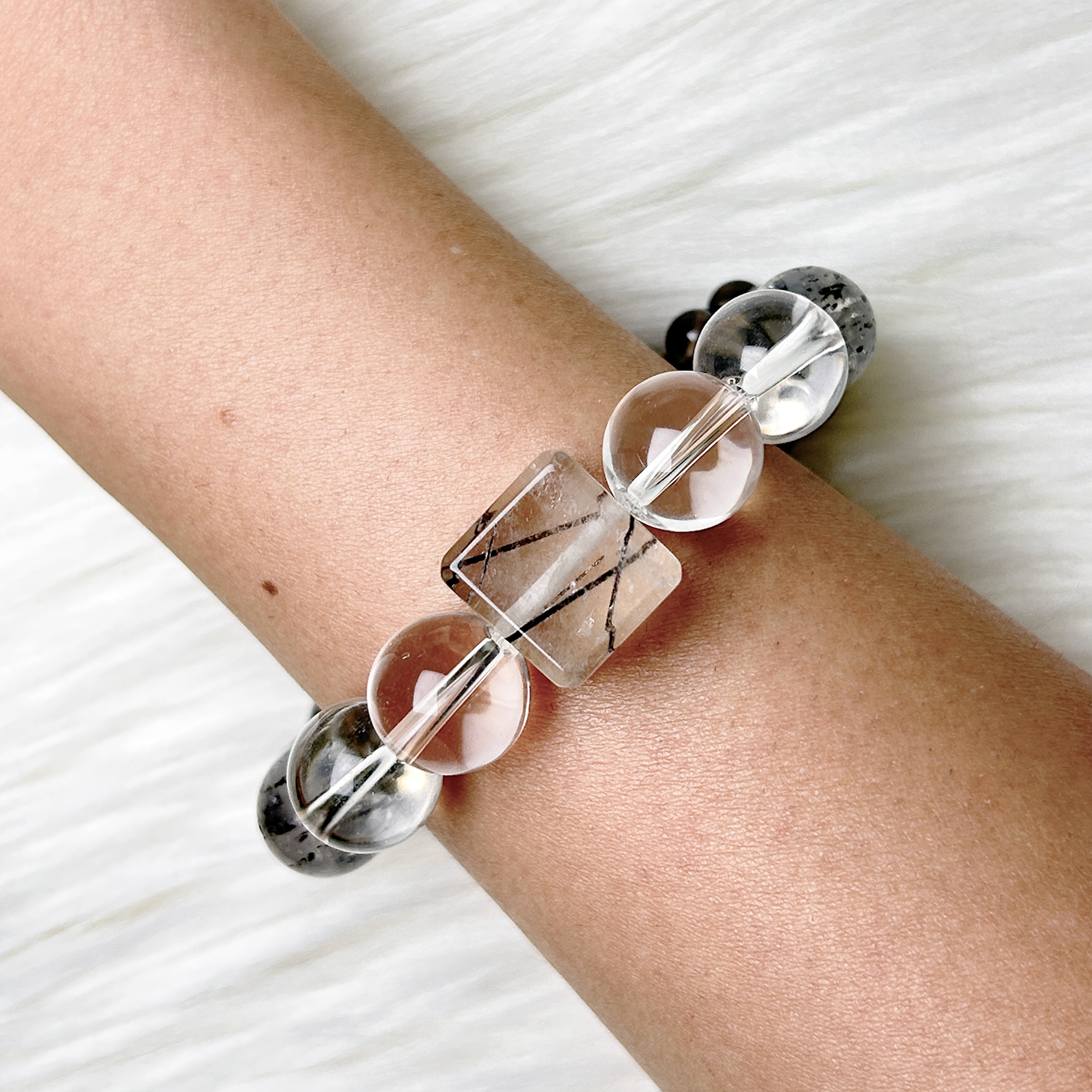 Monochrome Vein bracelet worn on wrist showing rutilated quartz centerpiece and gradient crystal tones from light to dark.