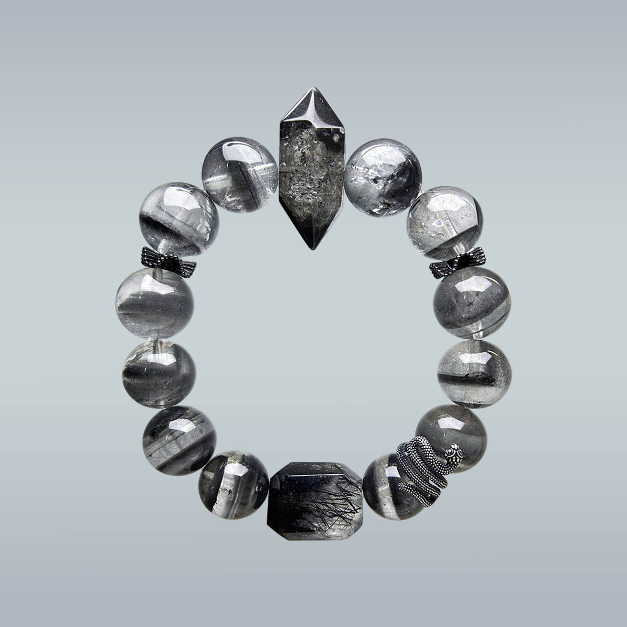 Full view of a Black Phantom Quartz and Rutilated Quartz bracelet with a double-terminated clear-black centerpiece, faceted black rutilated quartz bead, silver snake charm, and bow spacers on gradient background.