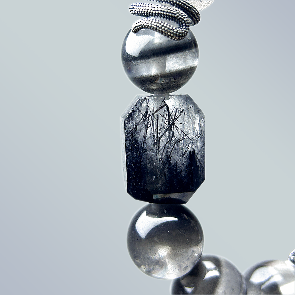 Close-up of faceted black rutilated quartz centerpiece with sharp needle-like inclusions, paired with reflective smoky quartz rounds and silver detailing.