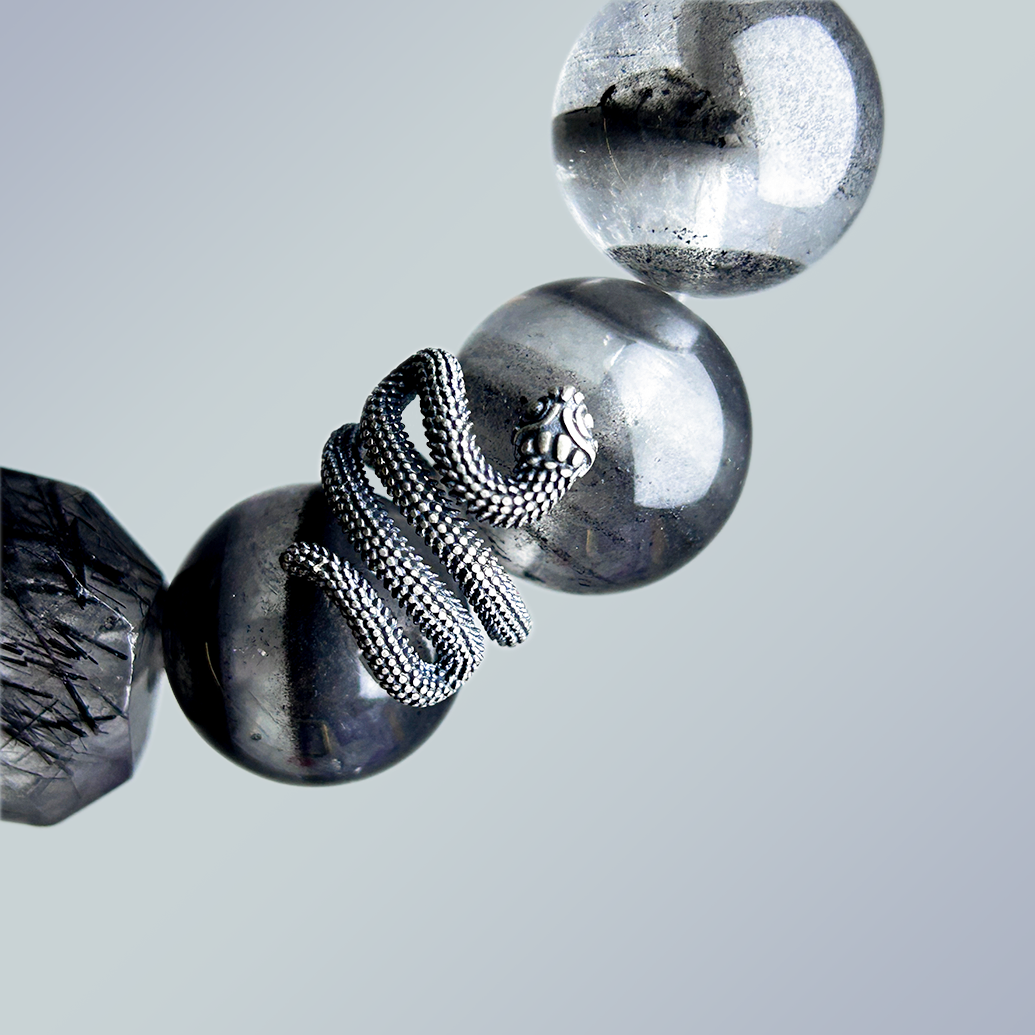 Macro close-up of the silver-tone snake charm wrapped around a polished Black Phantom Quartz bead, emphasizing the textured metal and gemstone clarity.