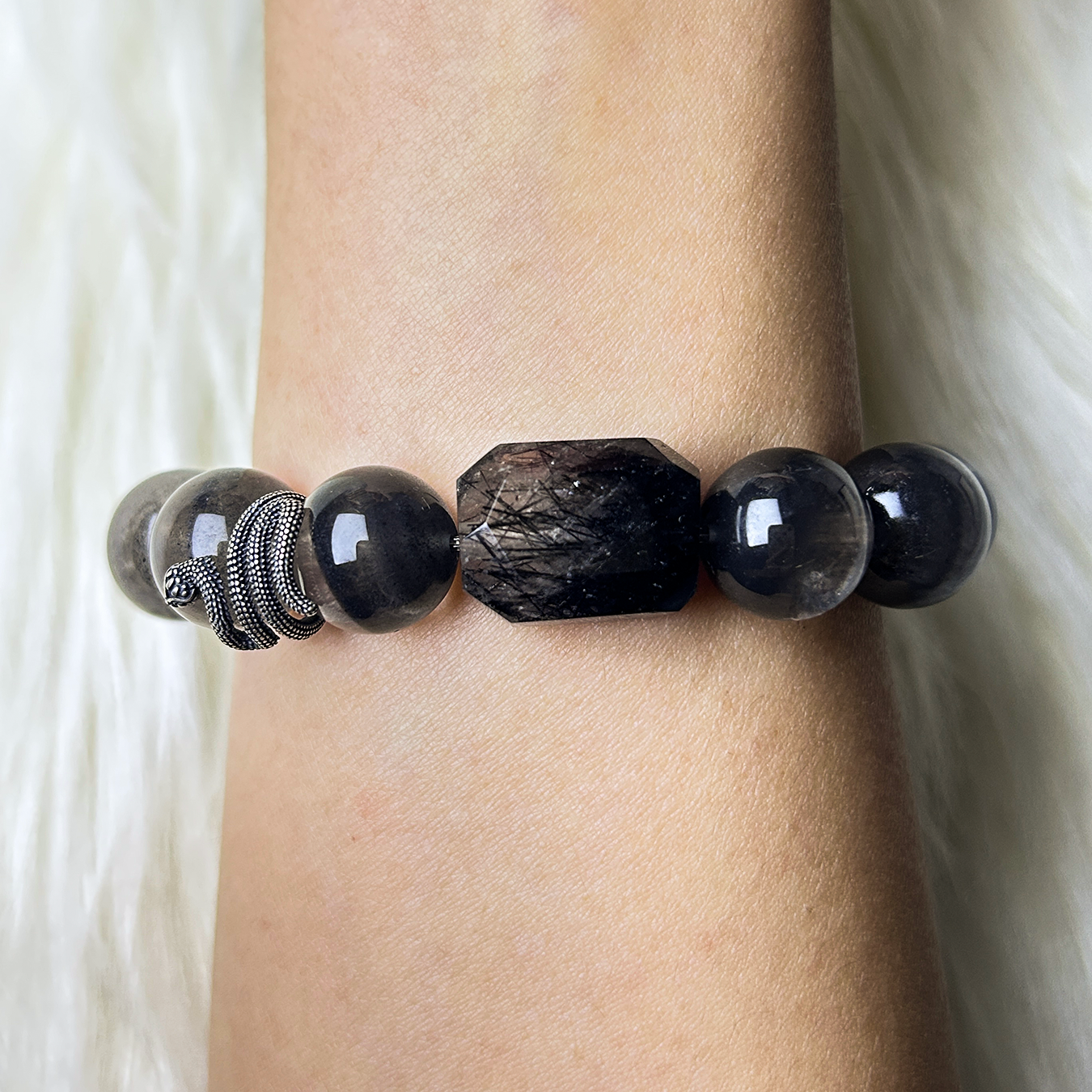 Wrist shot featuring the bracelet’s lower half, with a large faceted black rutilated quartz centerpiece and a silver snake charm accenting dark smoky beads.