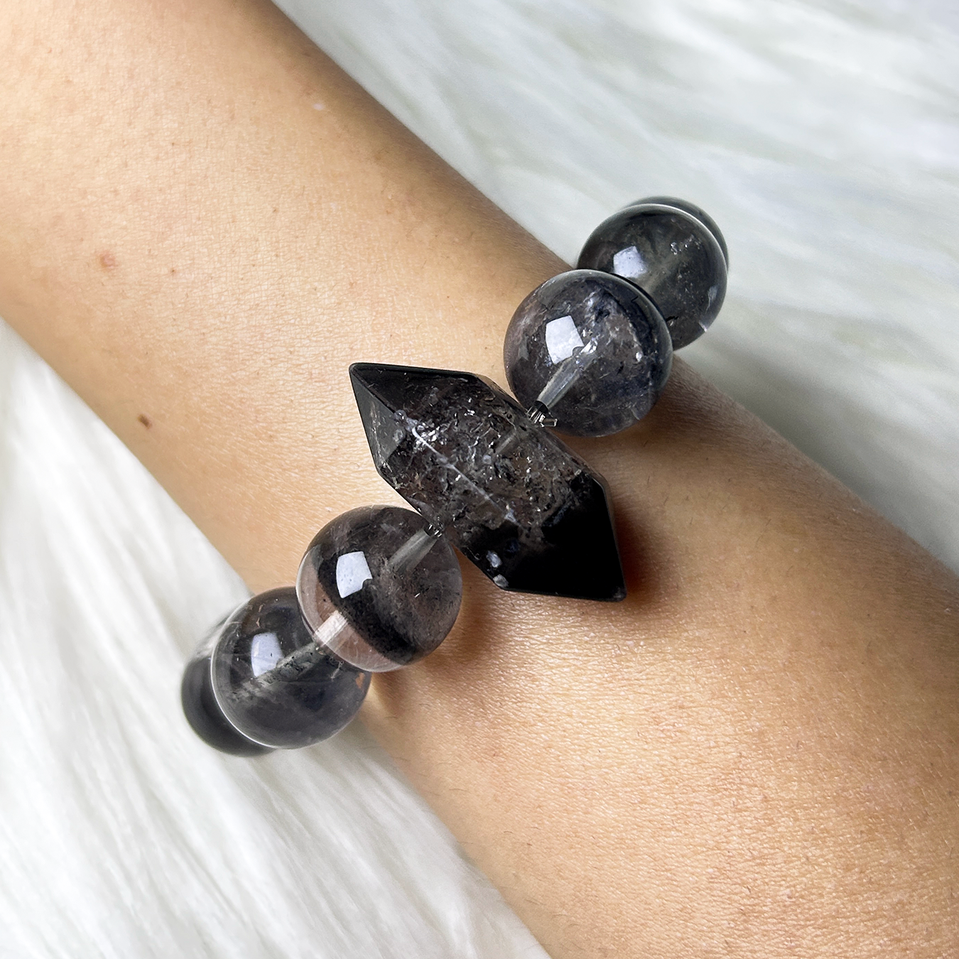 Angled wrist view highlighting the pointed double-terminated Rutilated Quartz centerpiece and glossy black phantom beads.