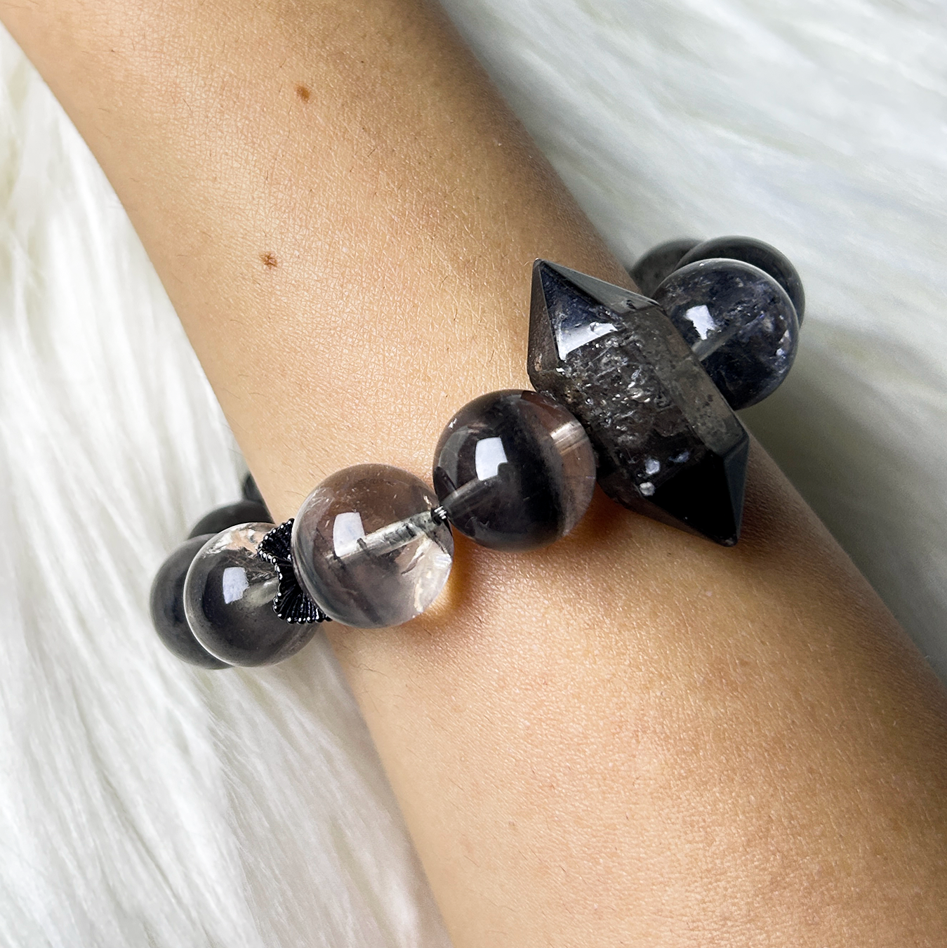 Wrist shot of the bracelet showing the smoky Black Phantom Quartz beads and sharp double-terminated Rutilated Quartz centerpiece, emphasizing high-contrast layering.