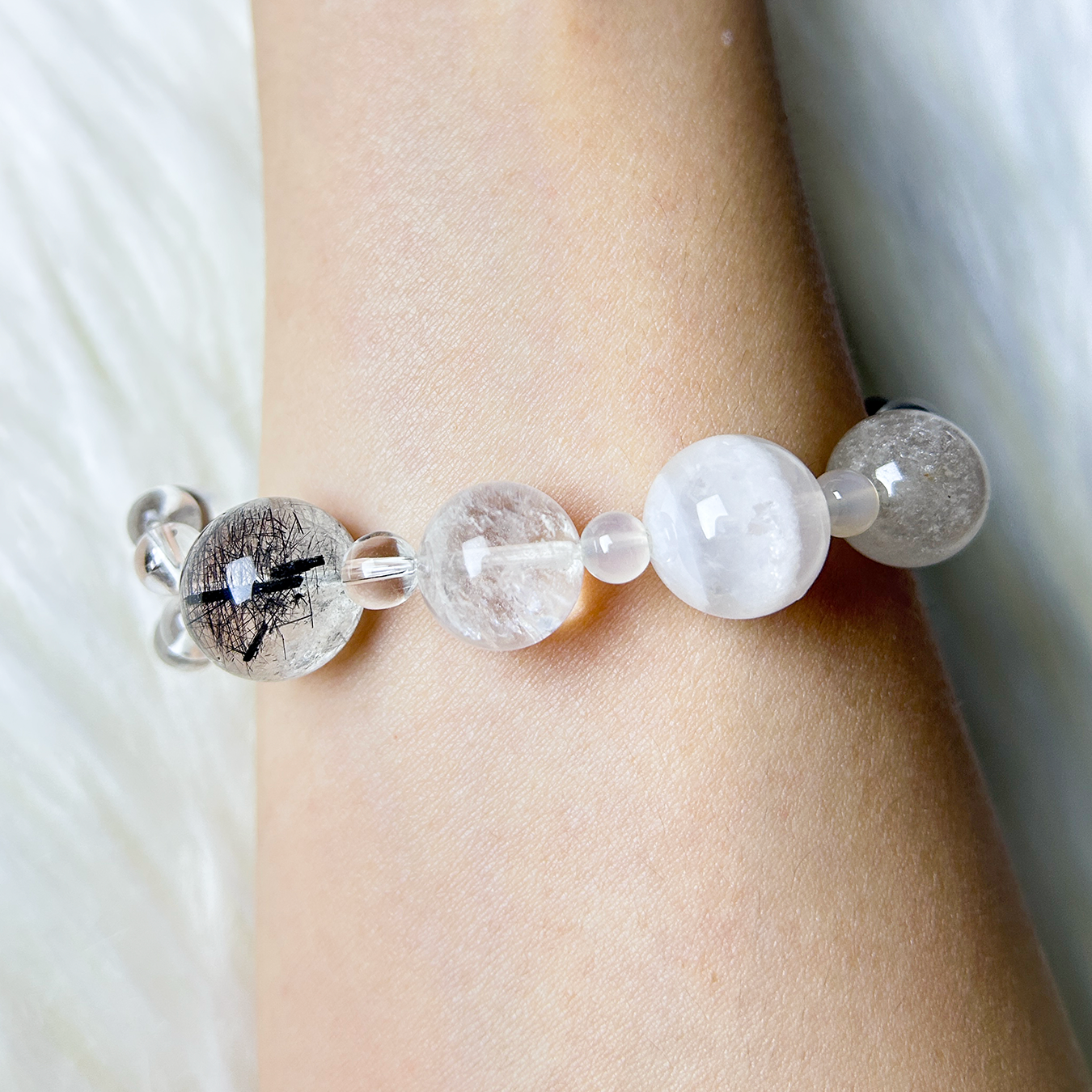Handmade crystal bracelet with rutilated quartzs, white azeztulite quartz, and white phantom quartz beads on wrist.