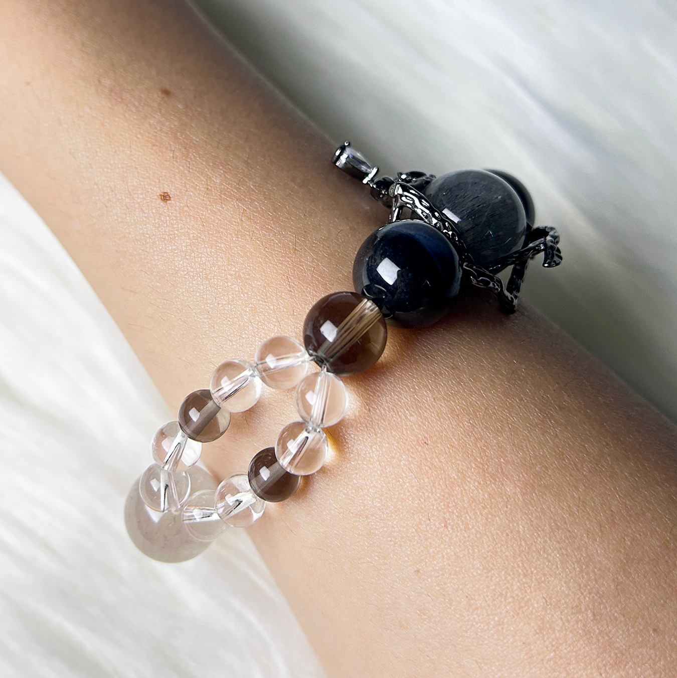Side view of a crystal bracelet on a wrist, showcasing Blue Tiger’s Eye, Clear Quartz, and Smoky Quartz with a black centerpiece charm, exuding mystical charm.