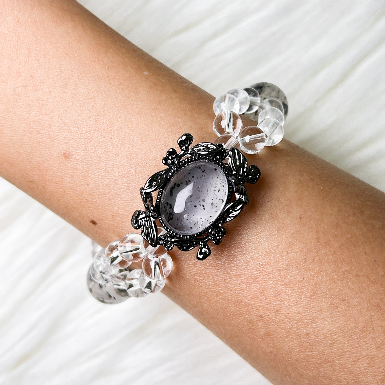 Noir Mist bracelet worn on wrist with ornate floral setting and layered clear-quartz beads