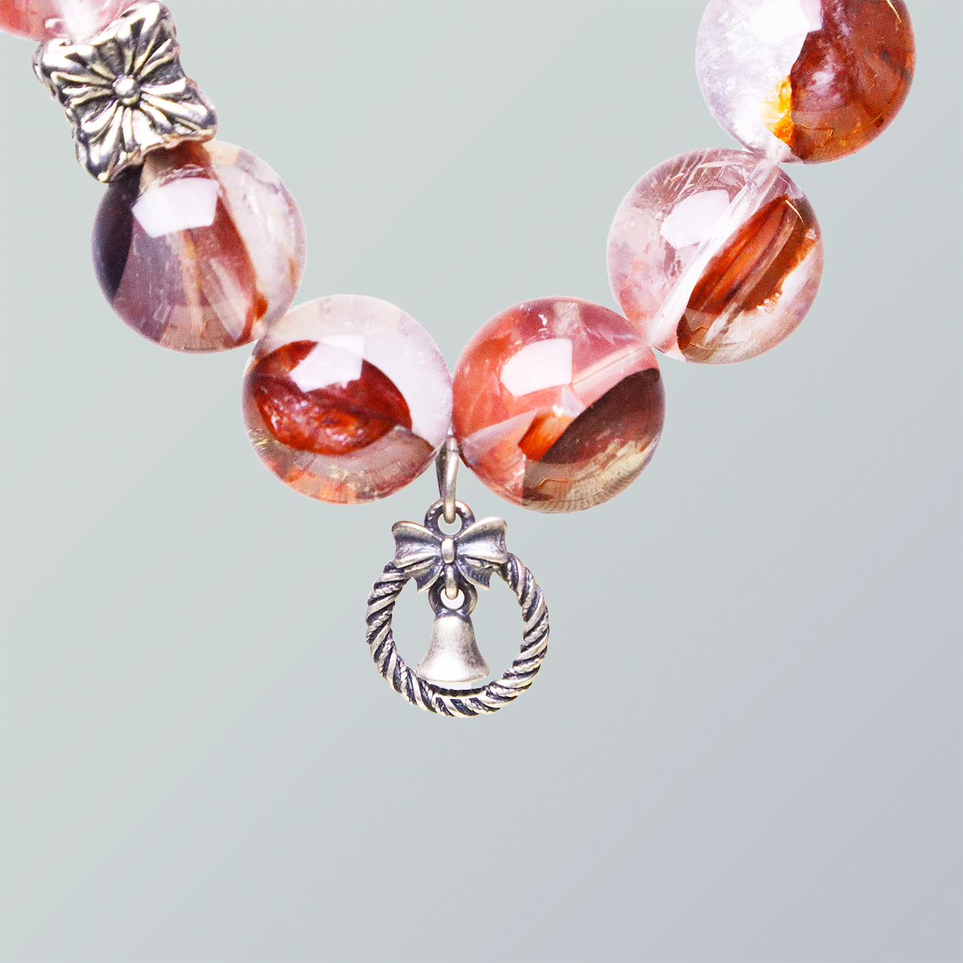 Detailed view of Hematoid Quartz beads with a silver bell and bow charm pendant, showcasing the gemstone’s rich inner texture and warm hues.