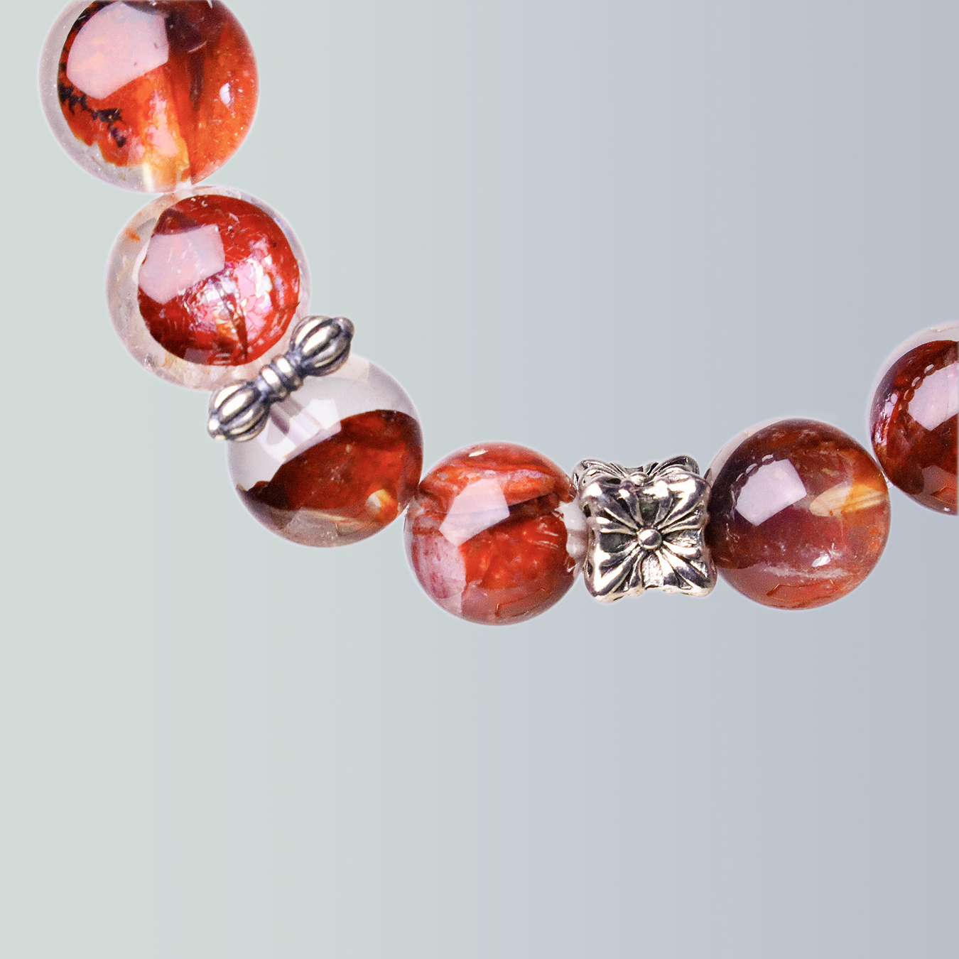 Close-up of Hematoid Quartz bracelet featuring vibrant red inclusions, a silver butterfly charm, and a flower-shaped metal spacer on a soft gradient background.