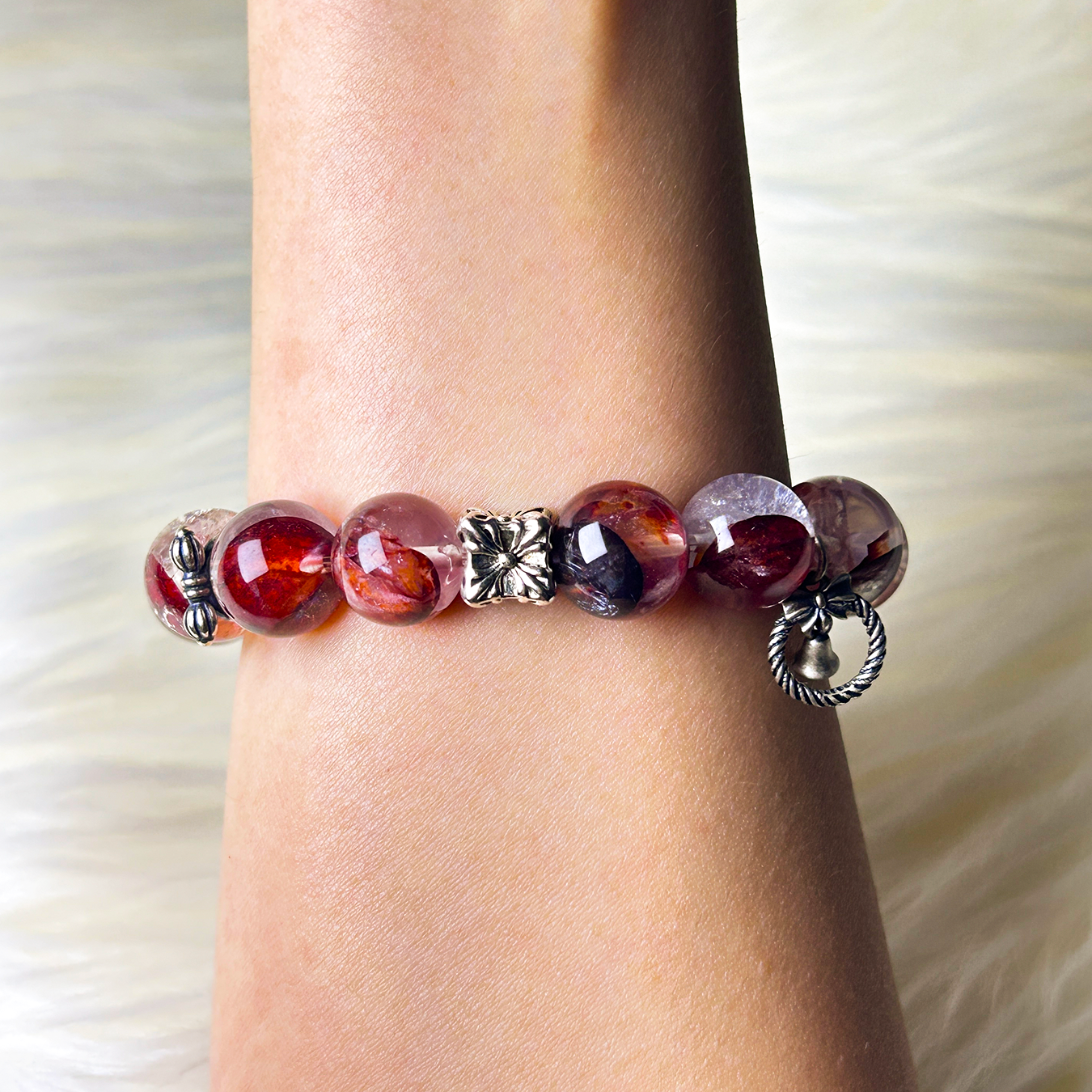 Top-down view of Hematoid Quartz bracelet worn on wrist, featuring a silver flower spacer, butterfly charm, and glossy red-orange crystal beads.