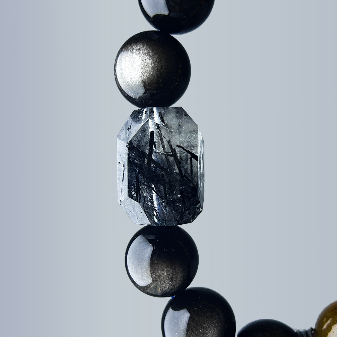 close-up of the octagonal black rutilated quartz centerpiece, flanked by silver cat’s eye beads, highlighting the needle-like inclusions inside the quartz.