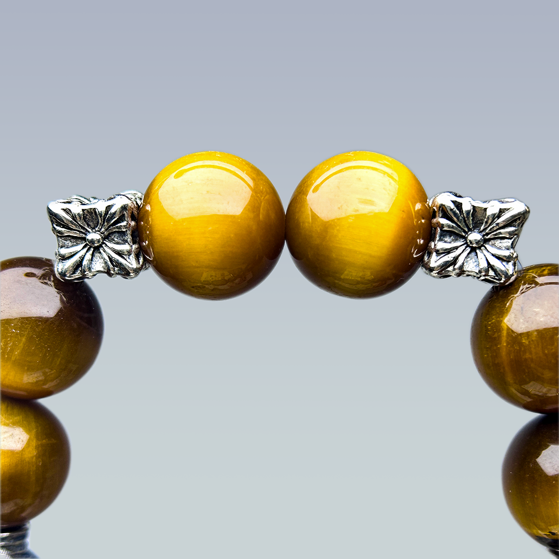 Macro view of two bright golden yellow tiger’s eye beads framed by intricate silver floral spacer beads, showcasing vivid chatoyancy and craftsmanship detail.