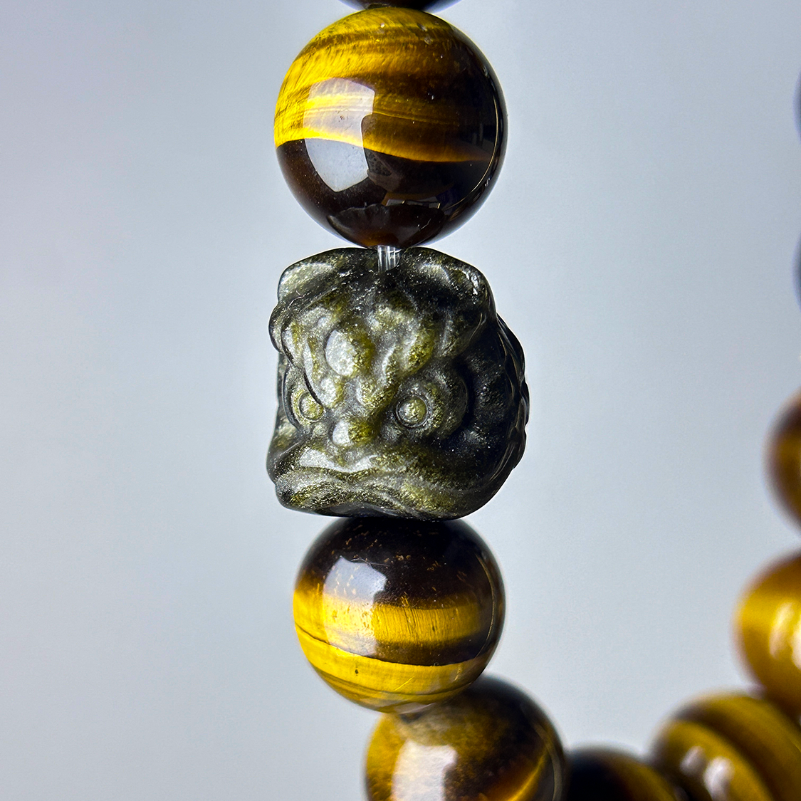 Close up shot of the pi xiu golden obsidian centerpiece of a yellow tiger's eye bracelet for men