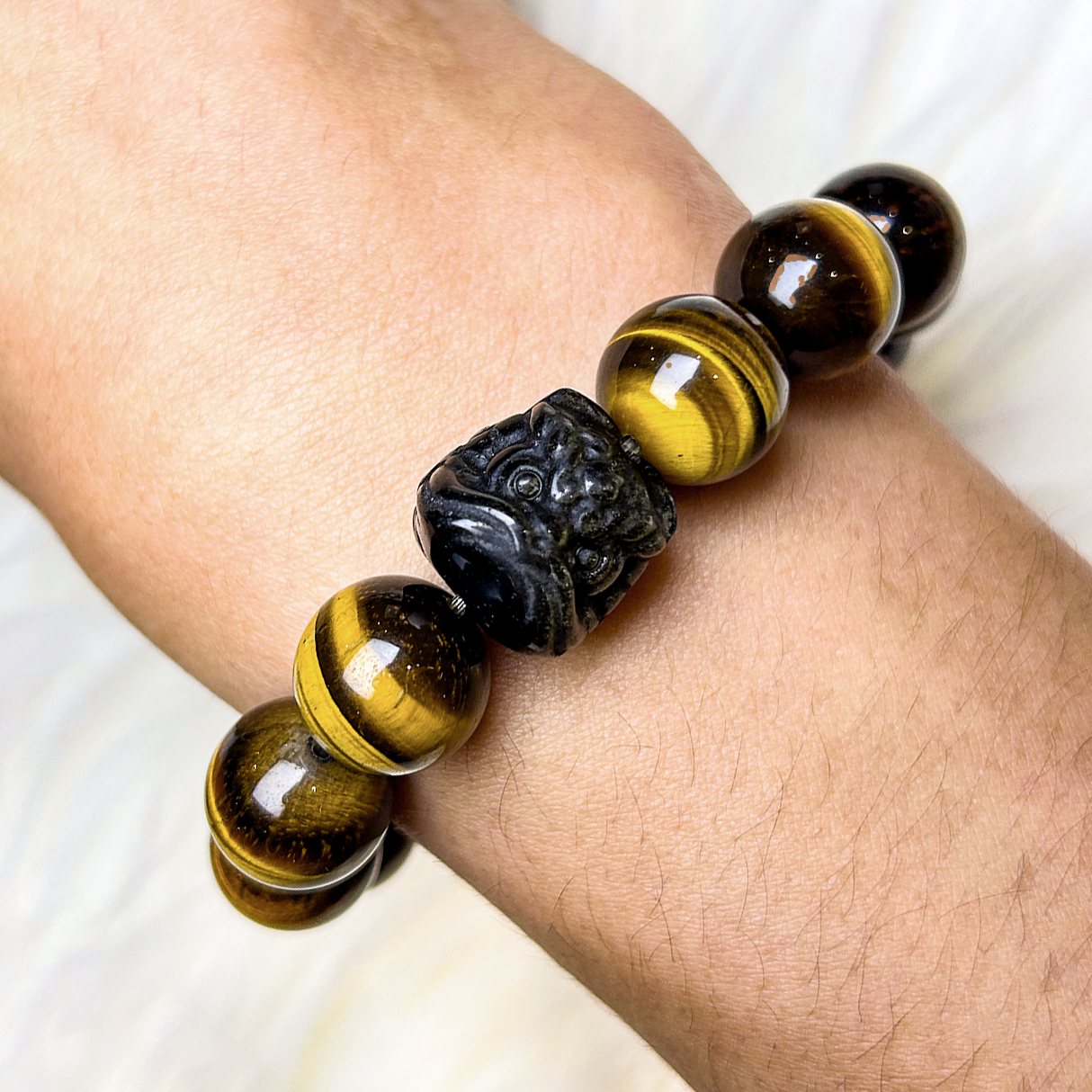 Close-up of men bracelet featuring golden yellow tiger’s eye, centered with a carved Pi Xiu charm for wealth protection.