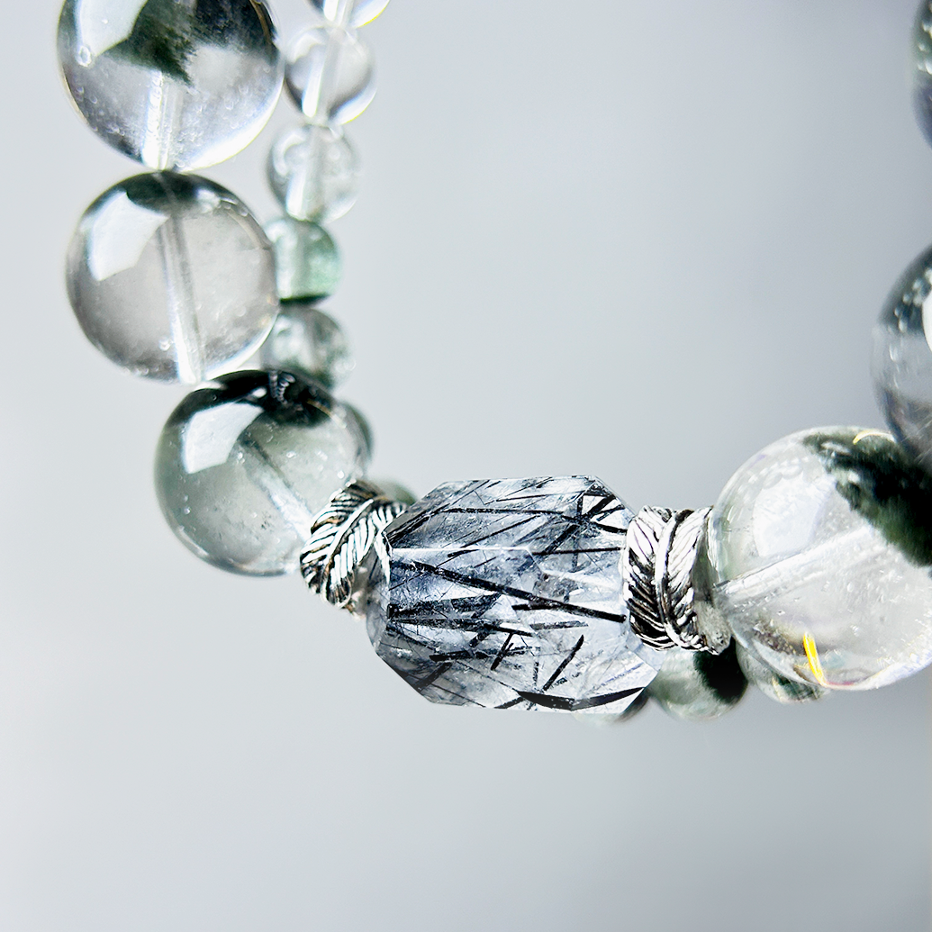 Close-up of hexagonal clear rutilated quartz bead framed with silver spacers between Green Phantom Quartz beads