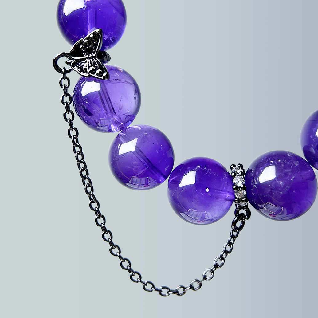 Close-up of the bracelet's back design, highlighting polished dark amethyst rounds and a black butterfly charm with attached safety chain.