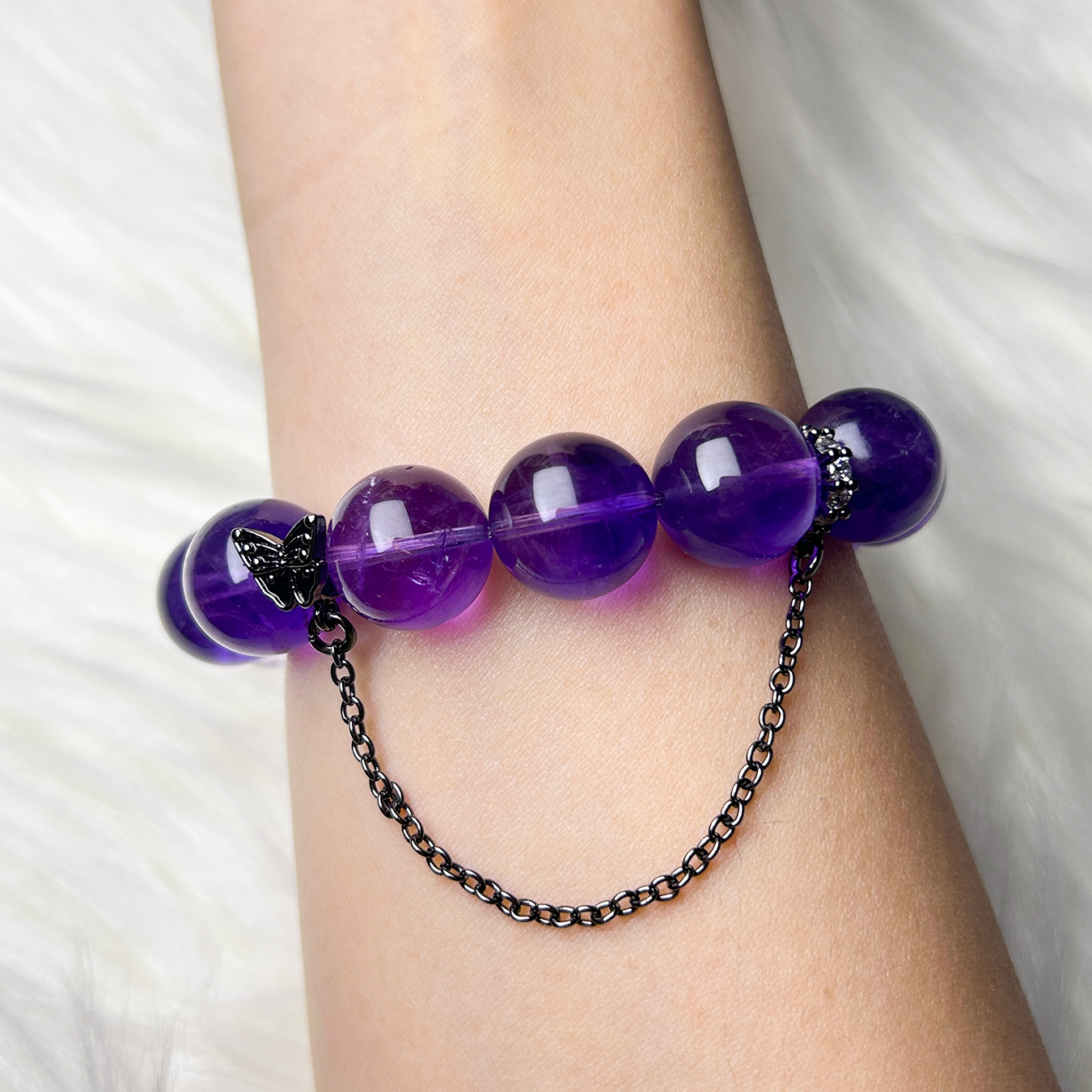Rear view of the bracelet on wrist, showing polished round dark amethyst beads and a delicate black butterfly chain charm for added elegance.