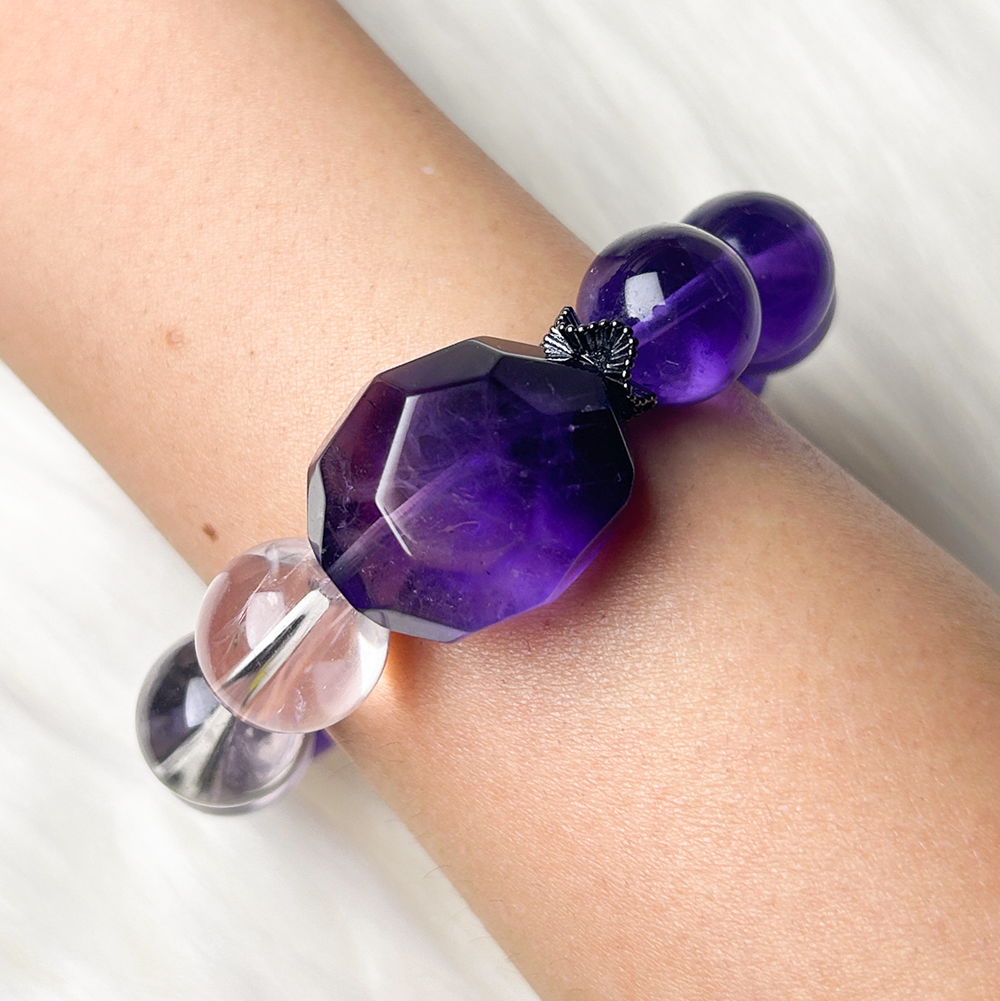 Top view of faceted dark amethyst centerpiece surrounded by light and dark amethyst beads on wrist, highlighting the gradient color blend and gemstone cut.