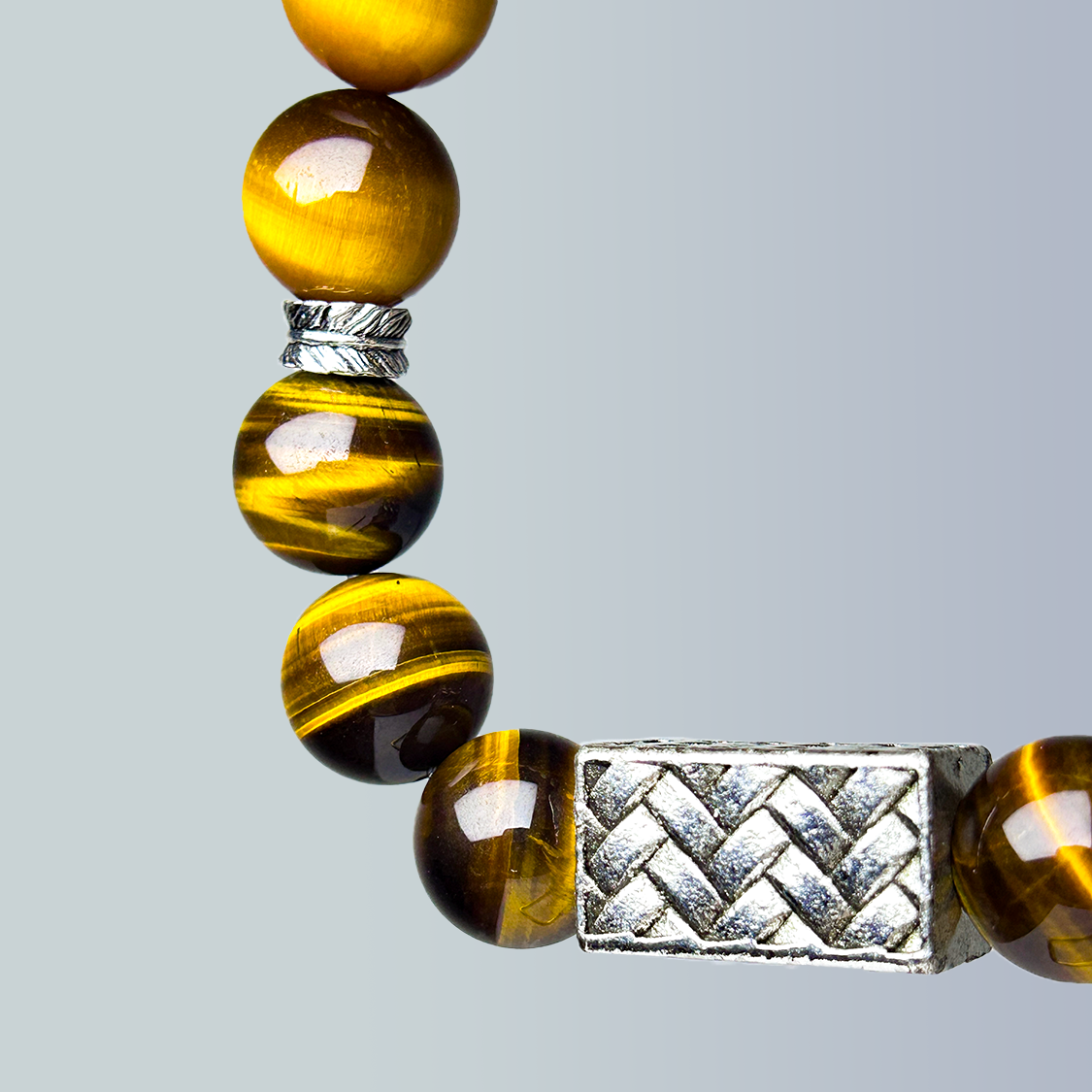 Beaded bracelet with yellow tiger eye beads and silver braided charms on a light gray background