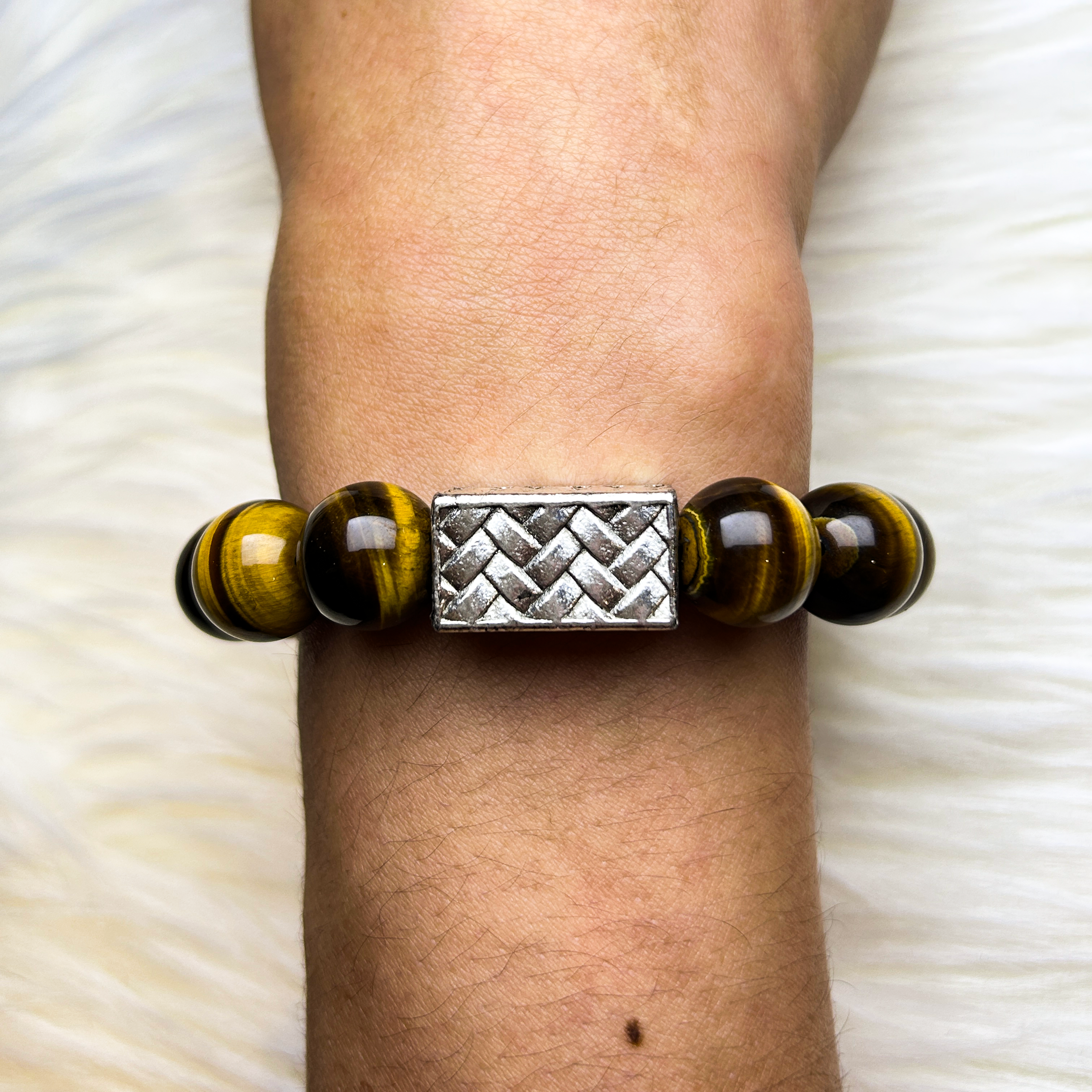Bracelet with yellow tiger eye beads and silver centerpiece on a wrist against a white background